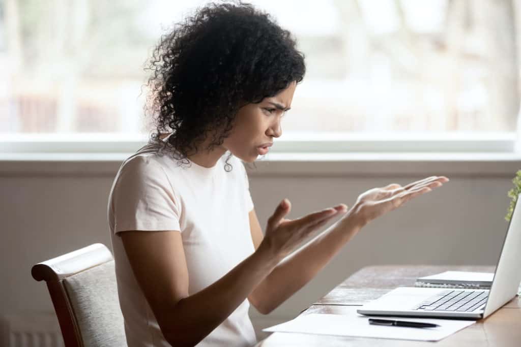 Woman at a lap top, palms open to the ceiling, brow furrowed, expressing frustration