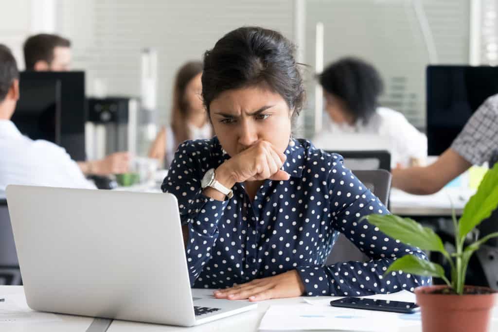 Worried businesswoman contemplating the total cost of fraud on her laptop