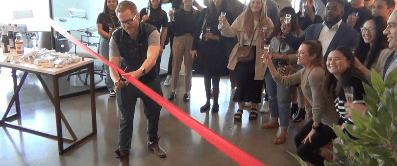 Signifyd Chief Customer Officer J. Bennett cuts the ribbon to officially open Signifyd's New York office in One World Trade Center. Signifyd employees raise Champagne glasses in celebration.