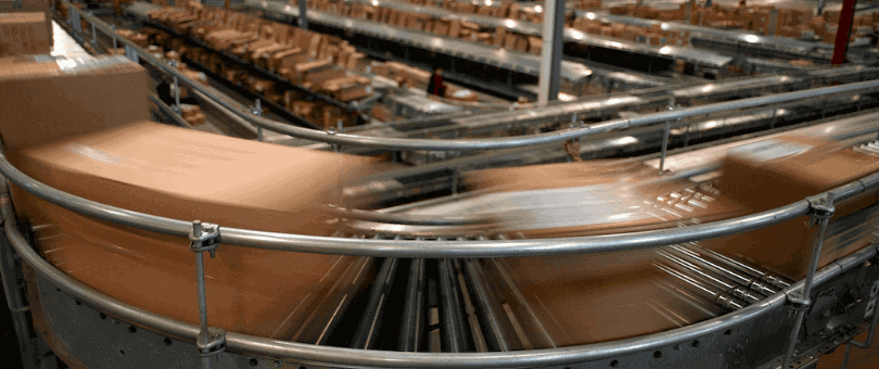 Ecommerce boxes on a speeding conveyor belt to symbolize the speed of ecommerce