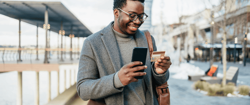 A man standing outside, making an online purchase with his smartphone and credit card