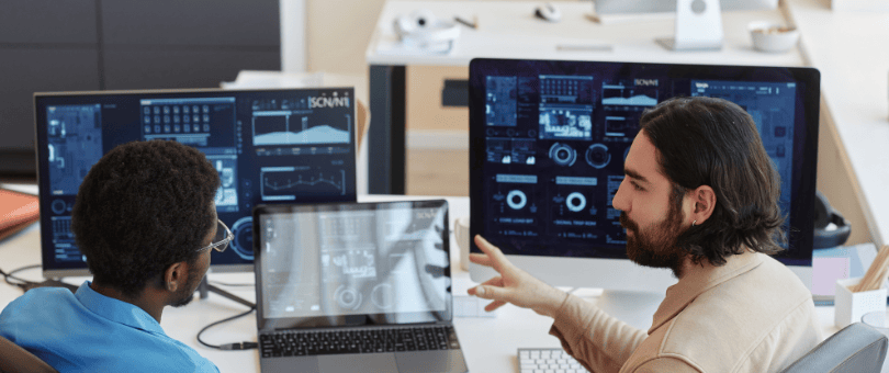 Two men in front of a bank of monitors, analyzing results